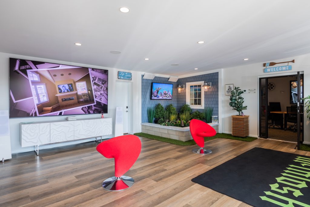 Outdoor audio showroom display with planter-style speakers, landscape audio, TV, lighting, and seating at SHORE Smart Home