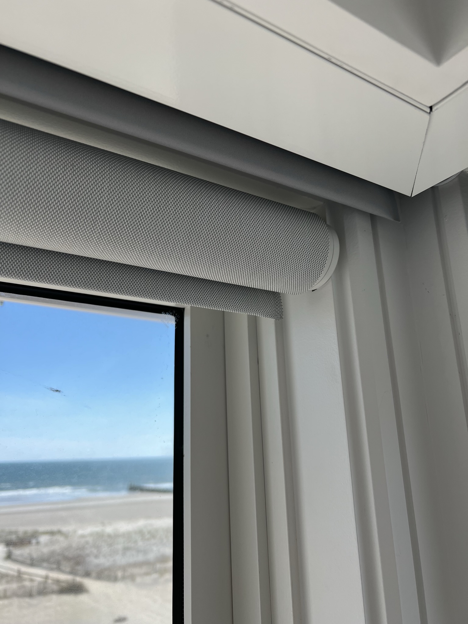 Recessed Lutron Sivoia QS blackout shades with exposed Palladiom roller shades in a beachfront home